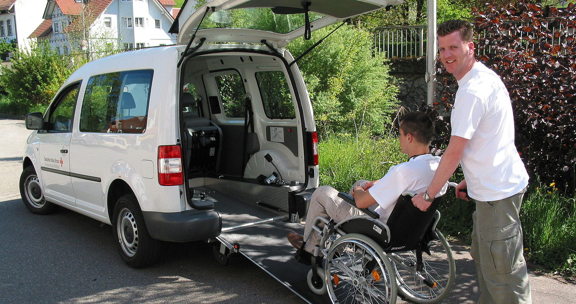 Ein Fahrer schiebt einen Rollstuhlfahrer in ein Auto mit Rampe
